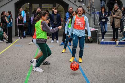 Des joueuses de l'Olympique de Marseille et des collégiennes disputent un match amical de football dans la cour de l'établissement, sous le regard attentif des spectateurs et du personnel encadrant. - Agrandir l'image 6 sur 16, fenêtre modale