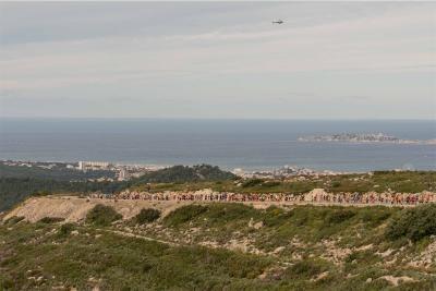 Vue panoramique du semi-marathon Marseille-Cassis avec une longue file de coureurs sur une route sinueuse en pleine nature, surplombant la mer Méditerranée et les îles au loin, avec un hélicoptère dans le ciel. - Agrandir l'image 9 sur 12, fenêtre modale