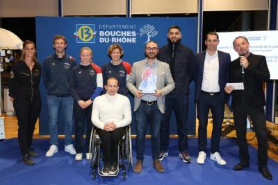 Groupe de personnes debout sur une scène avec le logo « Département Bouches-du-Rhône » en arrière-plan, dont une personne en fauteuil roulant, tenant un trophée artistique. - Agrandir l'image 4 sur 6, fenêtre modale