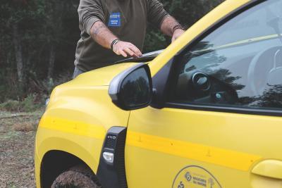 Personne en tenue de travail appuyée sur le capot d’un véhicule jaune marqué du logo « Forestiers Sapeurs » dans un environnement forestier. - Agrandir l'image 3 sur 6, fenêtre modale
