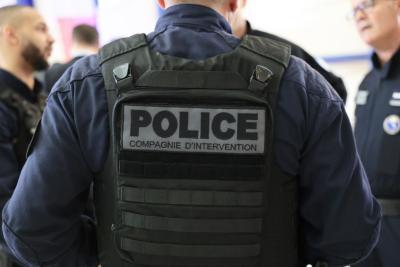 Un adulte vu de dos porte un gilet tactique noir marqué “POLICE COMPAGNIE D’INTERVENTION”. D’autres agents en tenue sombre sont visibles autour. Le lieu est un espace intérieur clair, évoquant un rassemblement officiel. Il s'agit de la cérémonie des voeux au personnel des forces de l'ordre et de secours des Bouches-du-Rhône. - Agrandir l'image 10 sur 18, fenêtre modale