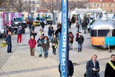 Espace extérieur où des visiteurs se déplacent entre stands, véhicules d’exposition et structures métalliques - Agrandir l'image 3 sur 20, fenêtre modale