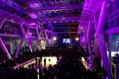 Vue d’ensemble d’un vaste hall éclairé en violet, rempli de participants lors d’un événement avec scène au fond - Agrandir l'image 6 sur 20, fenêtre modale