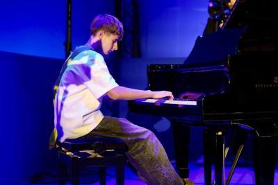 Jeune musicien jouant du piano à queue sur une scène éclairée en bleu durant un événement - Agrandir l'image 16 sur 20, fenêtre modale