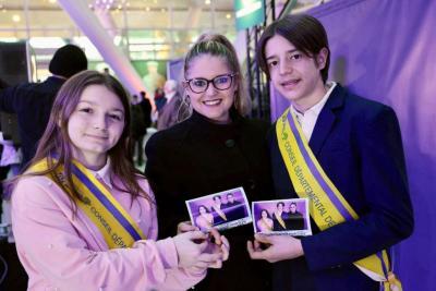 Trois jeunes portant des écharpes officielles et tenant des photos souvenirs lors d’un événement dans un hall lumineux - Agrandir l'image 7 sur 20, fenêtre modale
