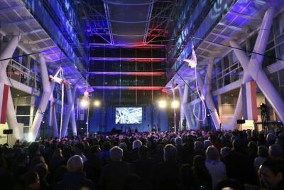 Vue d’un grand hall rempli de participants avec des acrobates suspendus et un écran de projection au fond - Agrandir l'image 13 sur 20, fenêtre modale