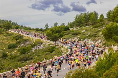 Grande foule de coureurs participant au semi-marathon Marseille-Cassis sur une route sinueuse bordée de végétation et de rochers, avec des collines verdoyantes en arrière-plan. - Agrandir l'image 7 sur 12, fenêtre modale