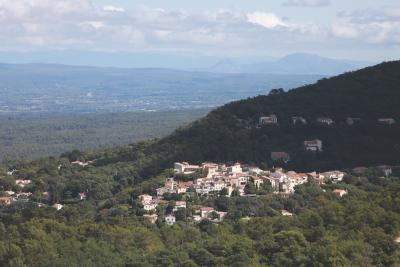 Un petit village est niché sur le flanc d’une colline boisée. À l’arrière-plan, on aperçoit une succession de collines et de montagnes sous un ciel partiellement couvert. - Agrandir l'image 4 sur 4, fenêtre modale