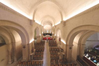 Intérieur d’une église ou chapelle avec de hauts plafonds voûtés. Des rangées de chaises en bois sont orientées vers un autel situé au fond. L’éclairage met en valeur les détails architecturaux, créant une ambiance calme et solennelle. - Agrandir l'image 4 sur 6, fenêtre modale