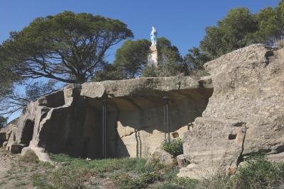 Statue blanche sur un piédestal, entourée d’arbres, dominant des roches taillées avec cavités et piliers métalliques, sous un ciel bleu. - Agrandir l'image 5 sur 6, fenêtre modale